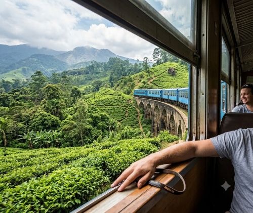 Looking out the window of the iconic blue train as it crosses a bridge surrounded by lush green tea plantations in Ella, Sri Lanka.